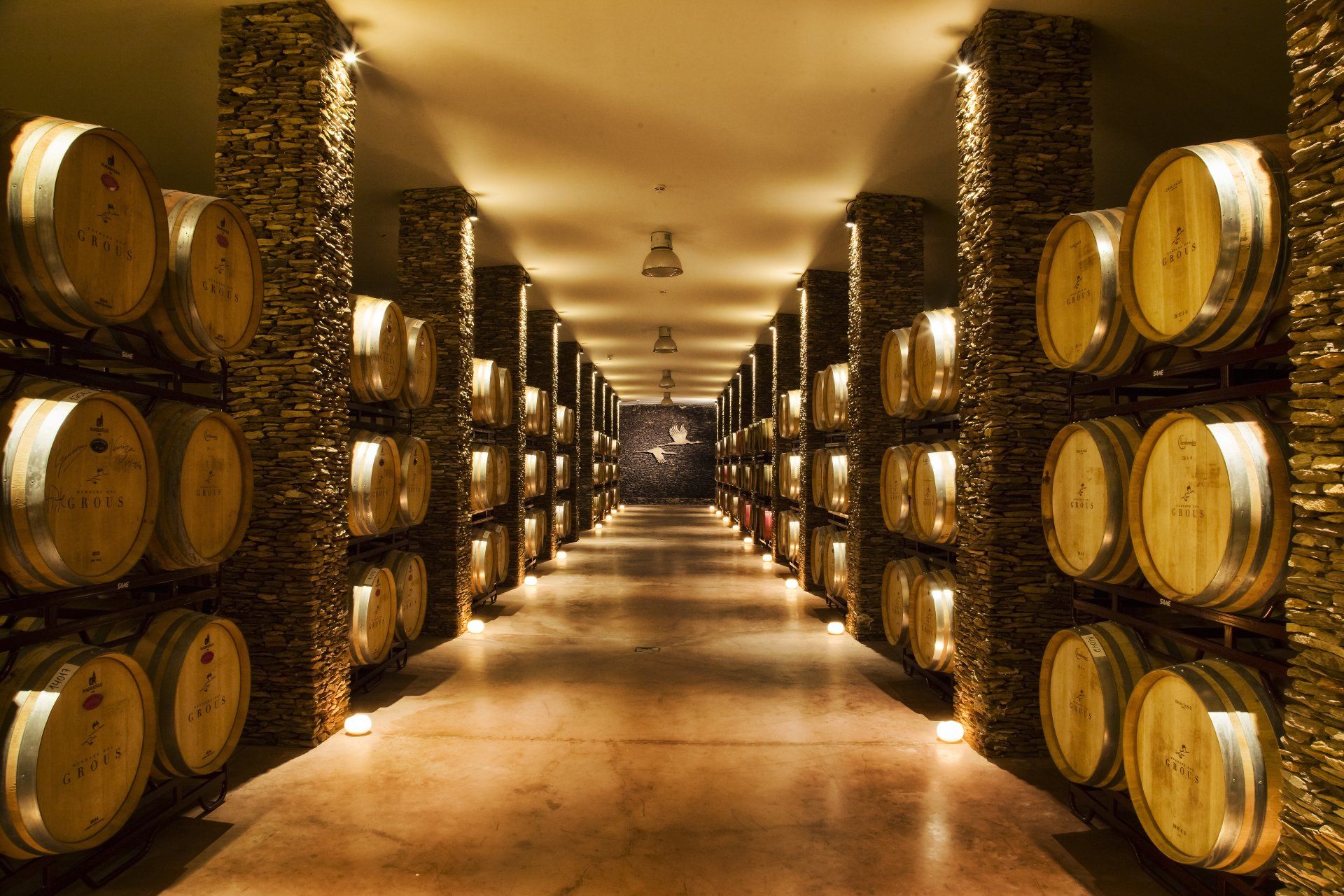 Wine barrels stored in a dimly lit cellar with stone walls.