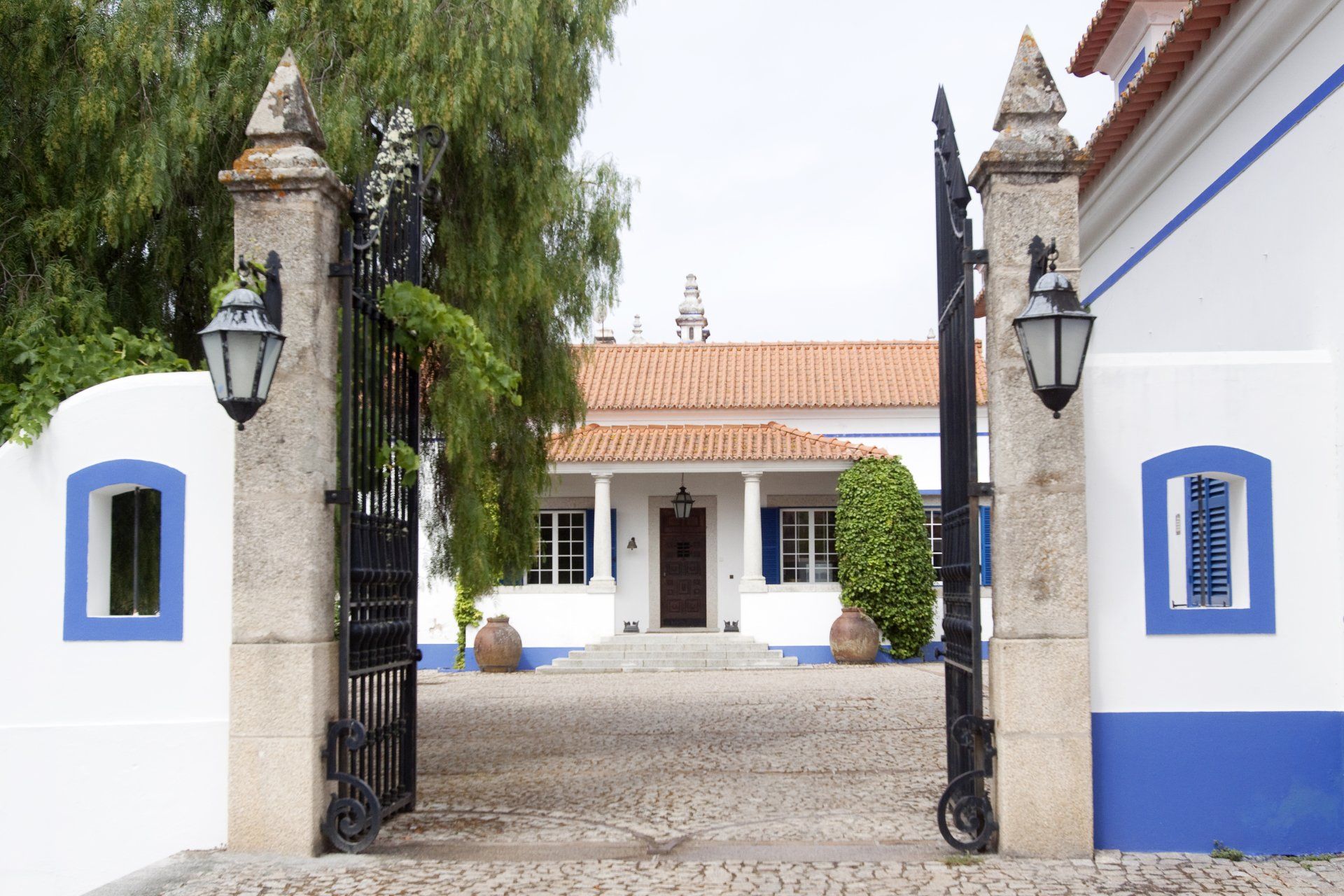 White and blue house entrance, iron gate, stone pillars, brick walkway.