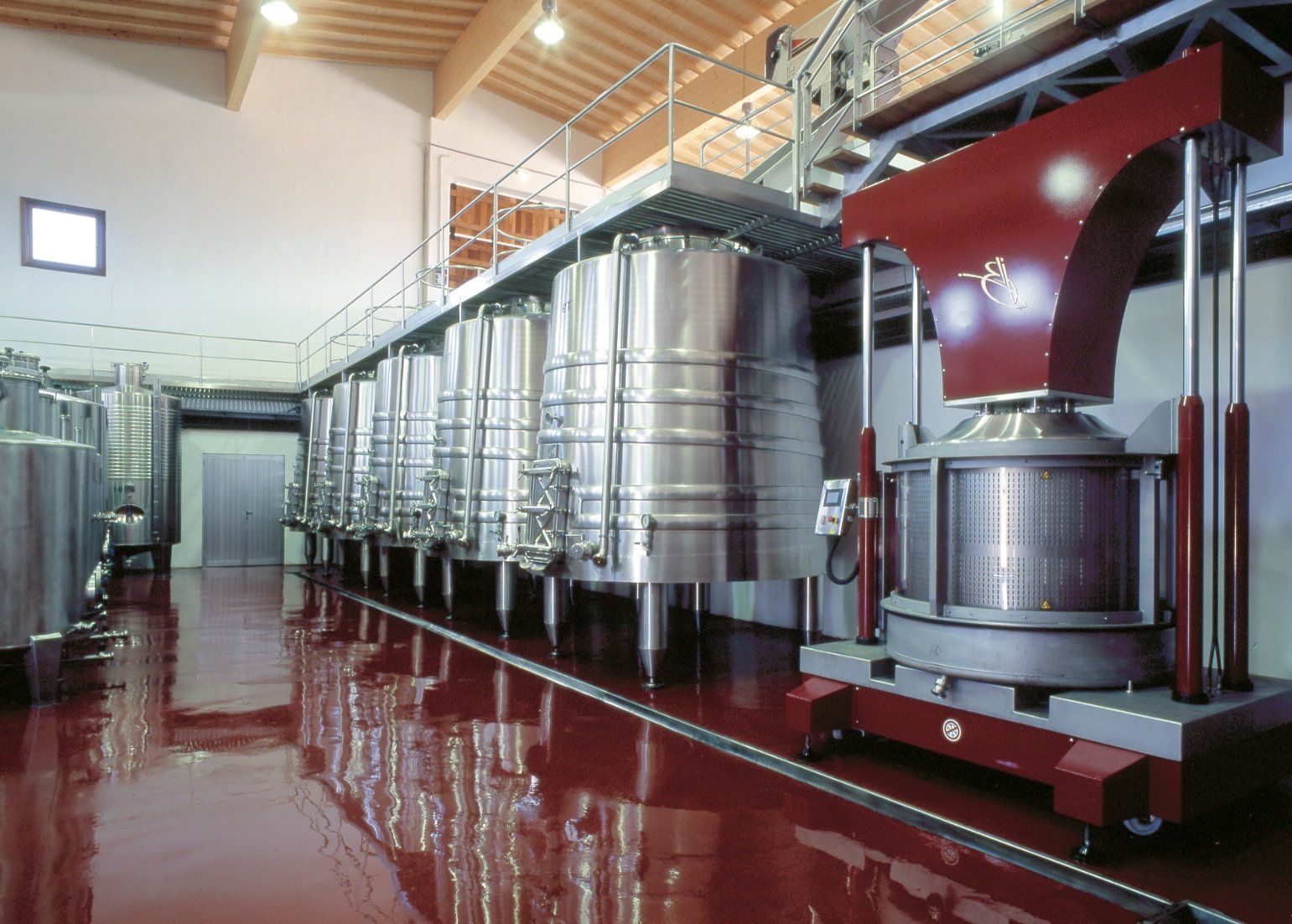 Wine production facility interior with stainless steel tanks and a press. Red floor.