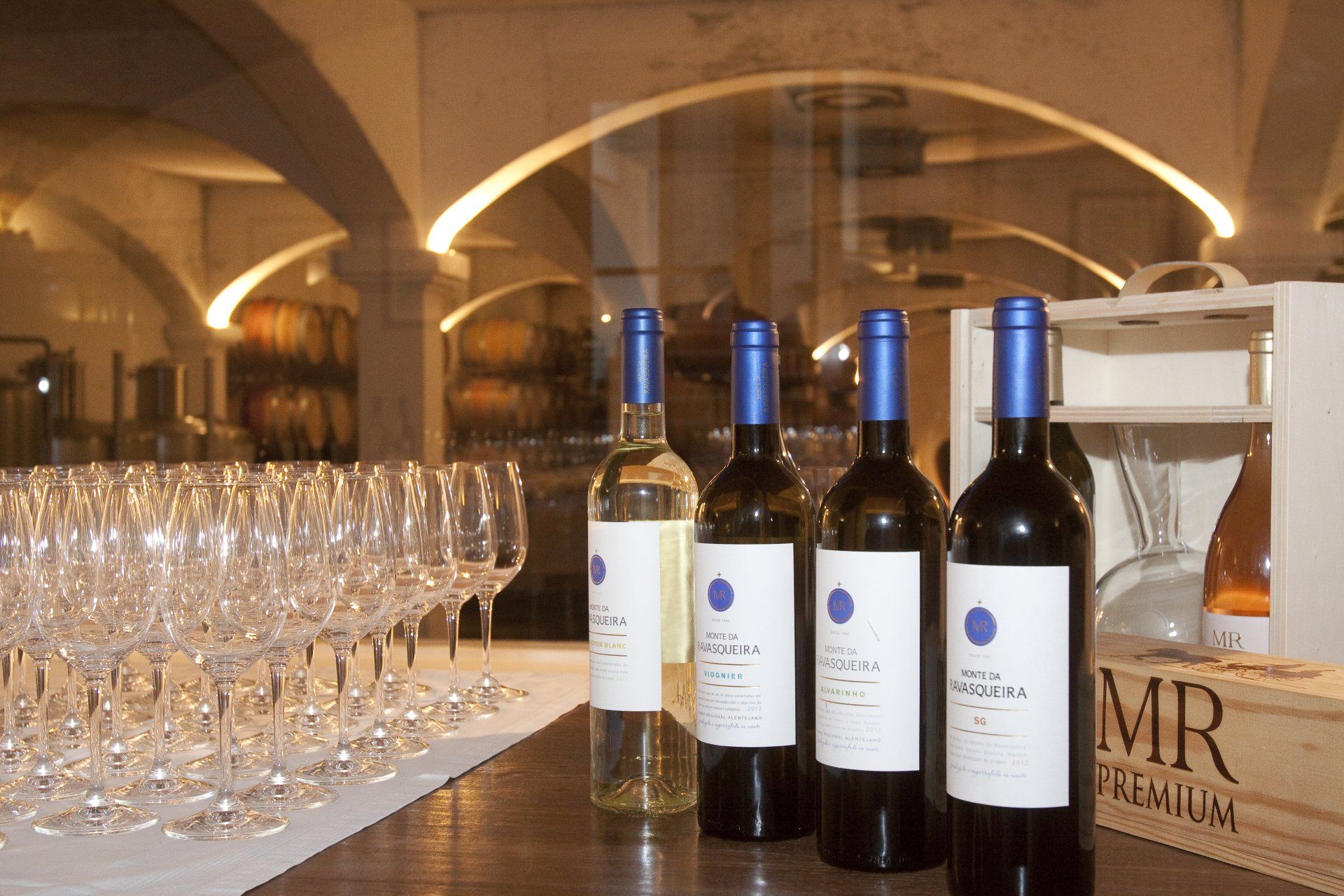 Wine bottles and glasses on a table in a cellar with arched ceilings.