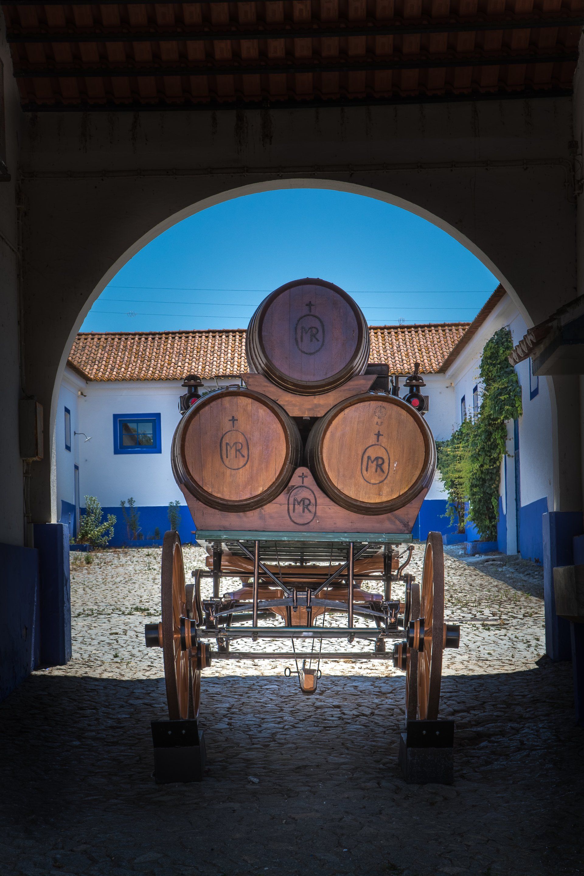 Wooden barrels stacked on a wagon under an arched doorway. Courtyard, blue sky.