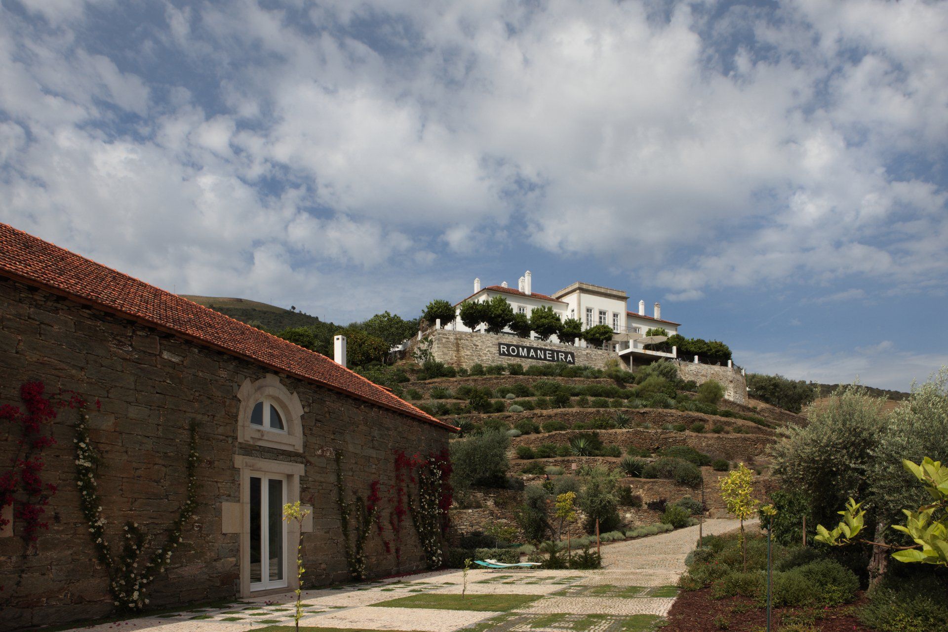 Stone buildings on a hillside with a mansion under a cloudy sky.