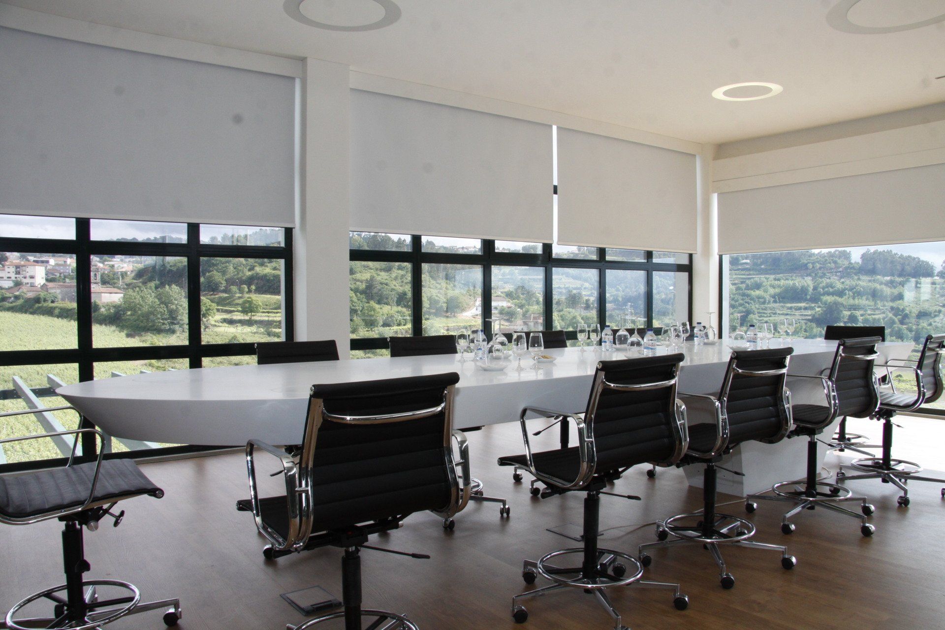 Conference room with long white table, black chairs, large windows, and outdoor view.