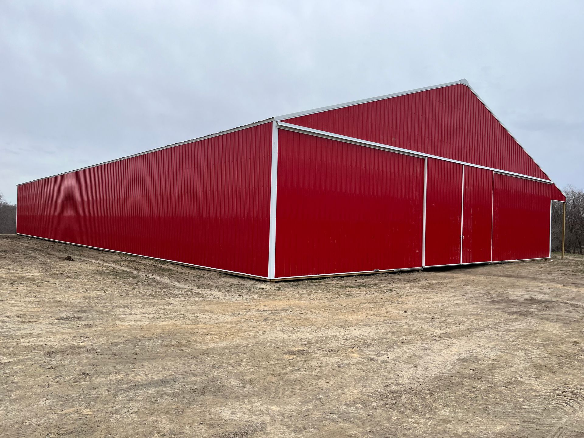 A large red barn is sitting in the middle of a dirt field.