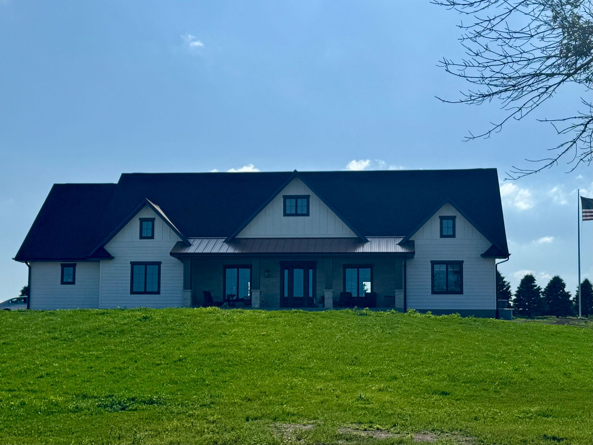 A white house with a black roof is sitting on top of a grassy hill.