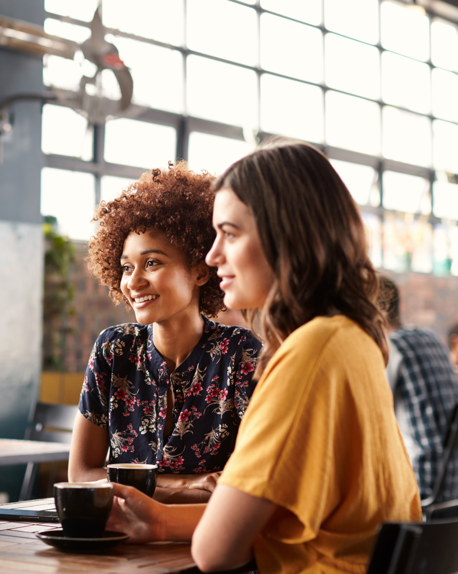Two women are sitting at a table in a restaurant drinking coffee.