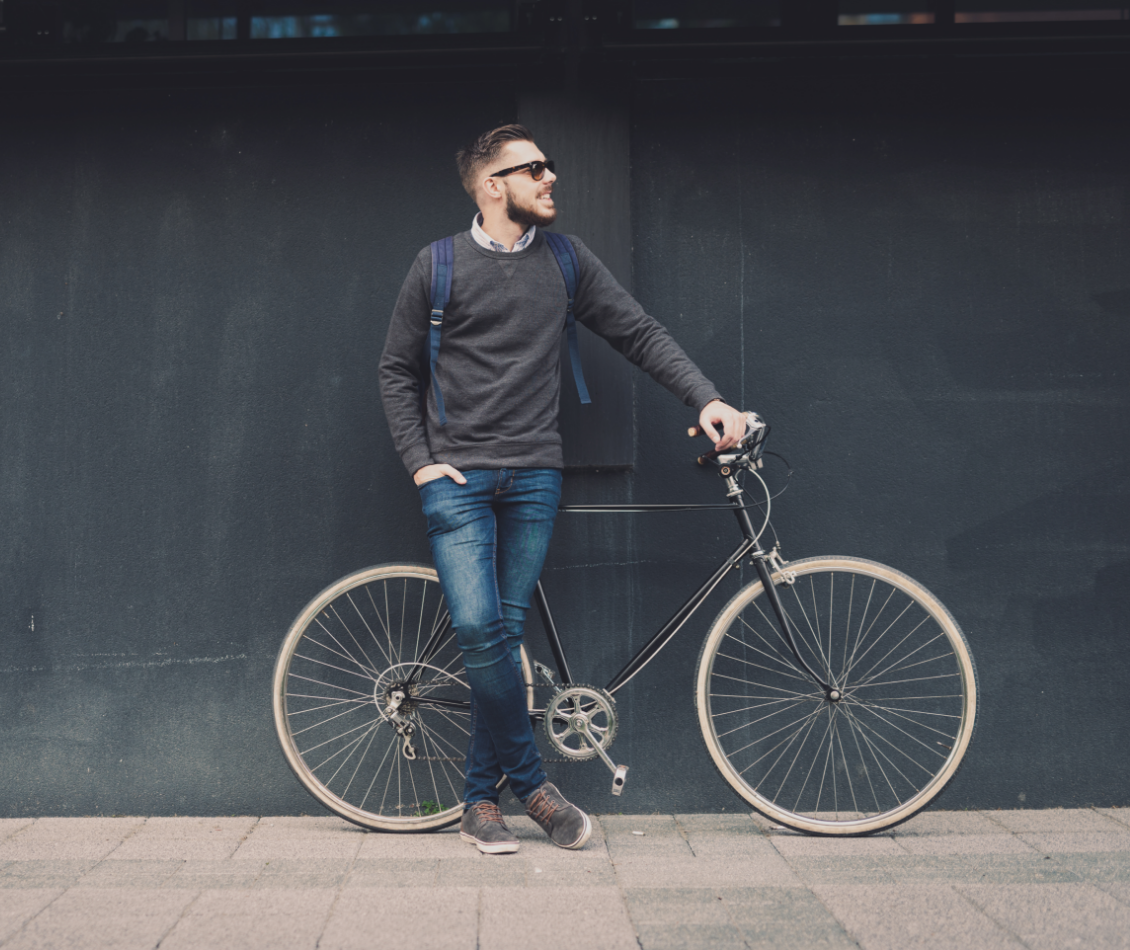 A man is standing next to a bicycle in front of a wall.