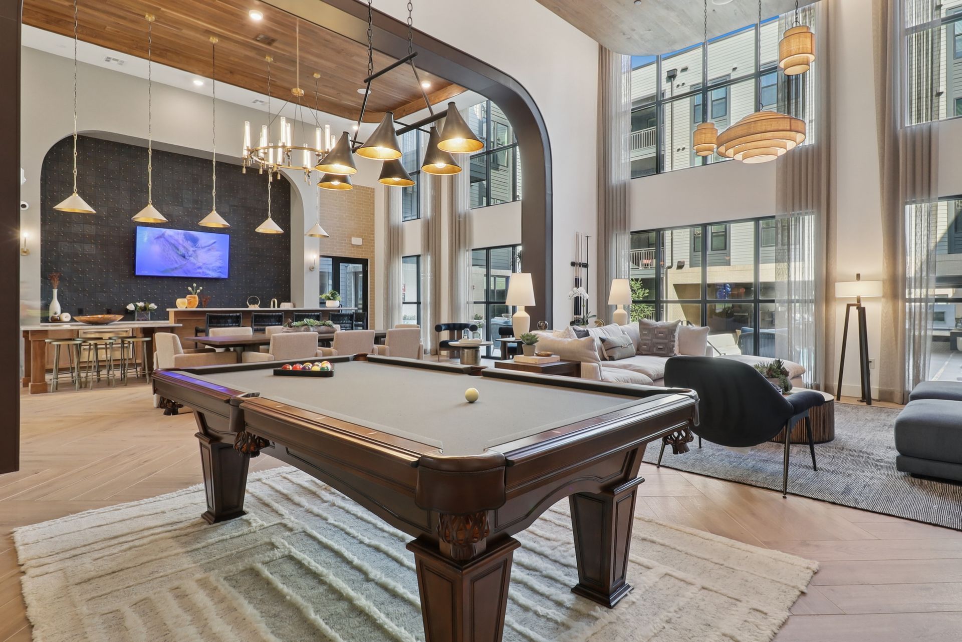 A well-lit, open-concept lounge area with a pool table, bar, and seating; floor-to-ceiling windows.