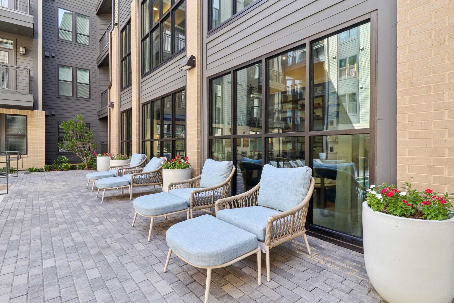 Outdoor patio with lounge chairs near a building with large windows and brick paving.