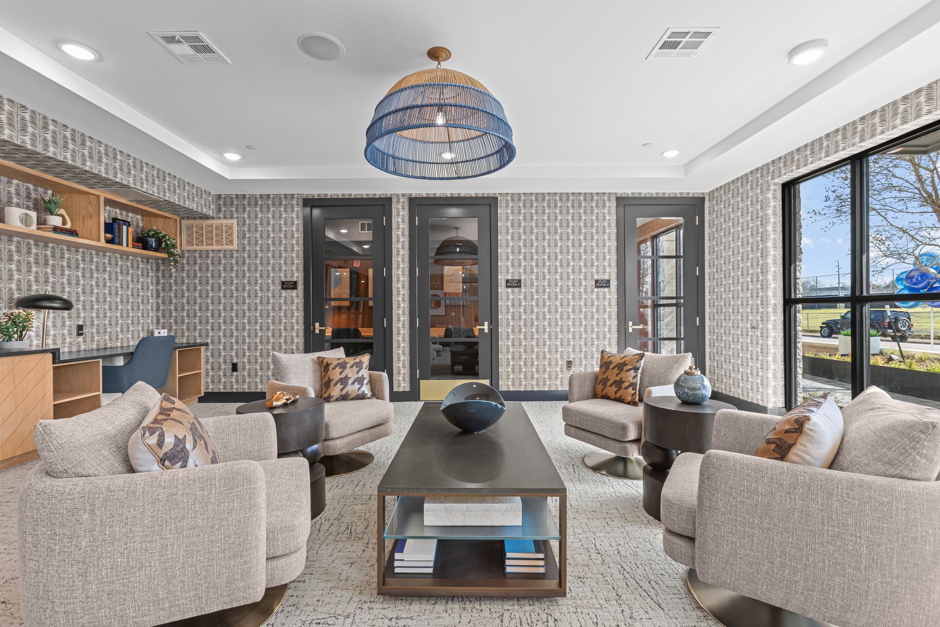 Cozy lounge area with patterned wallpaper, armchairs, coffee table, and large windows.