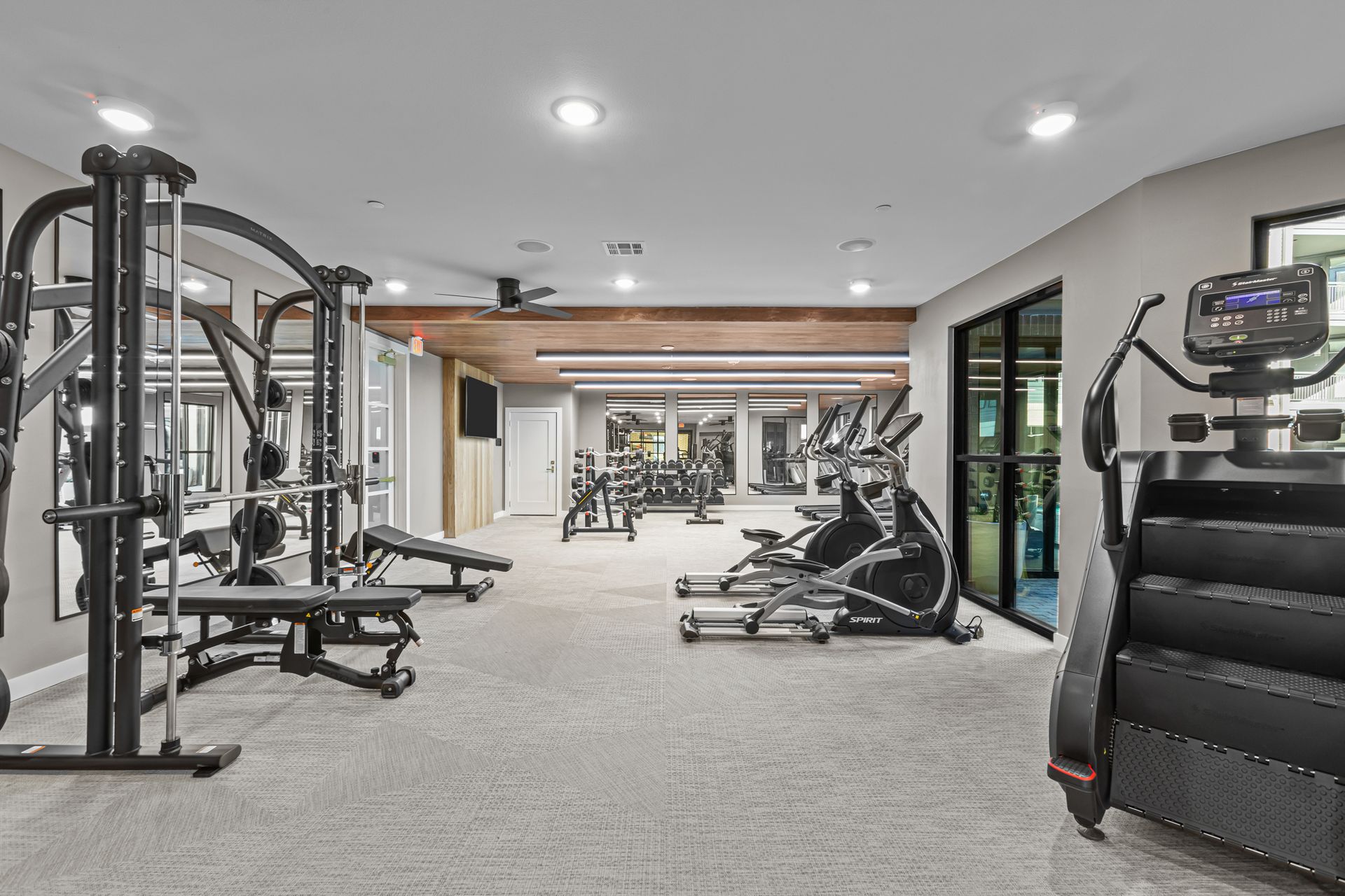 Gym with weight machines, treadmills, and stair climber; gray and white interior.