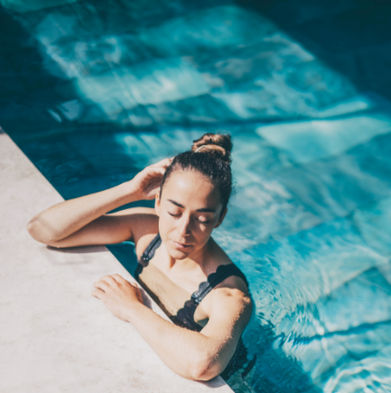 A woman is laying on the edge of a swimming pool with her eyes closed.