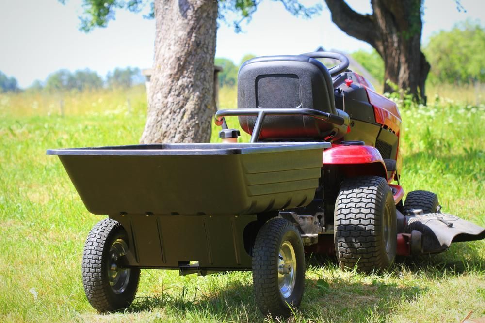 A Lawn Mower With A Trailer Attached To It Is Parked In A Grassy Field — Whitsunday Mowers In Proserpine, QLD