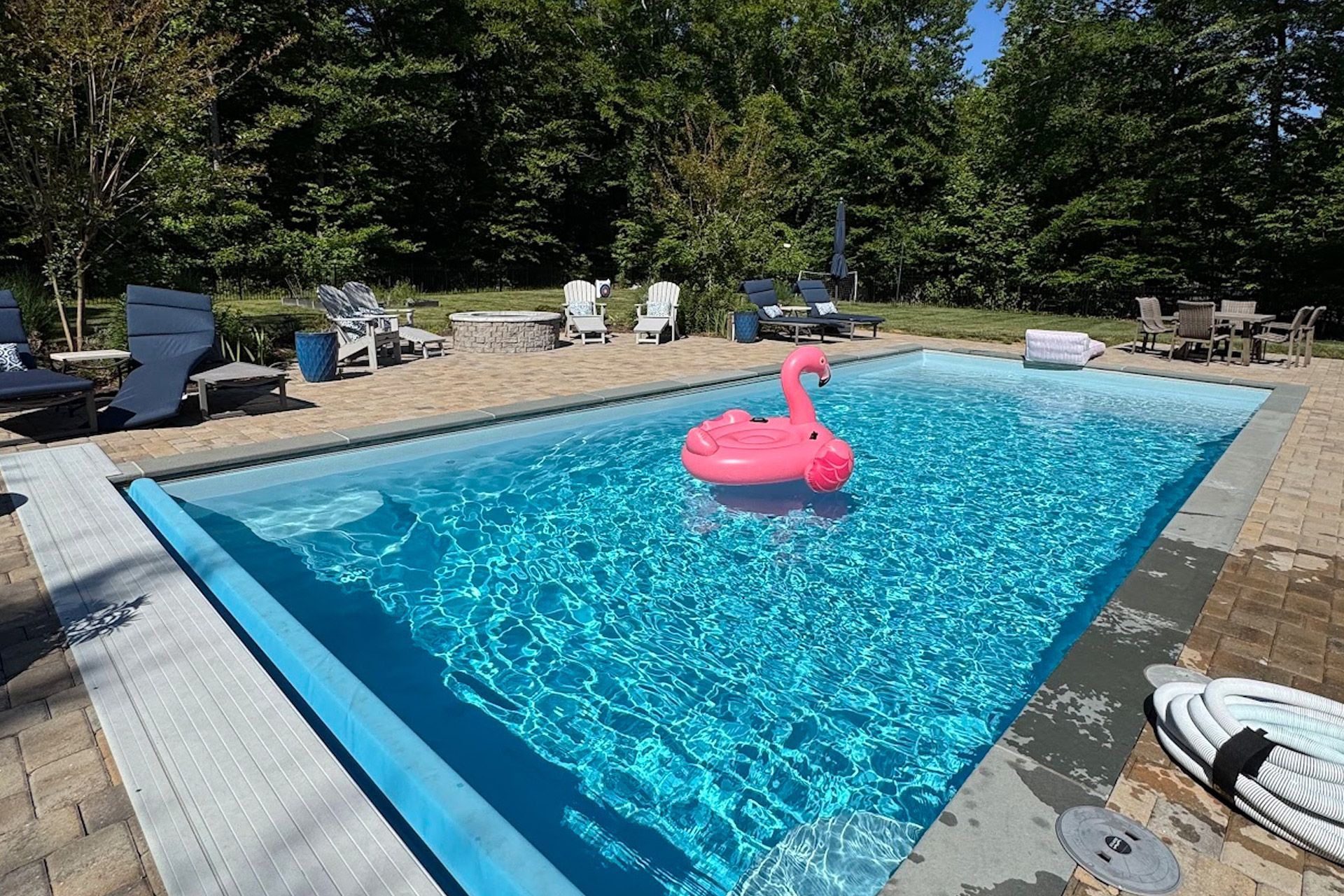 Rectangular backyard pool with dark water, white stone deck, and a covered patio in the background