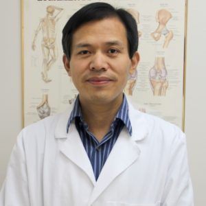 A man in a white coat stands in front of a poster of bones