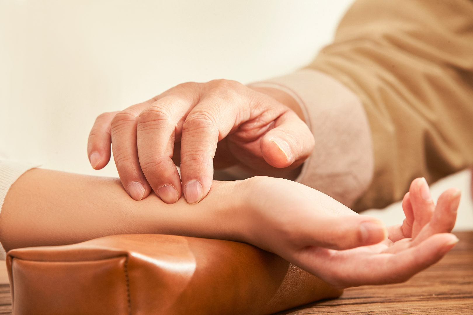 A person is taking a person 's pulse on a wooden table.