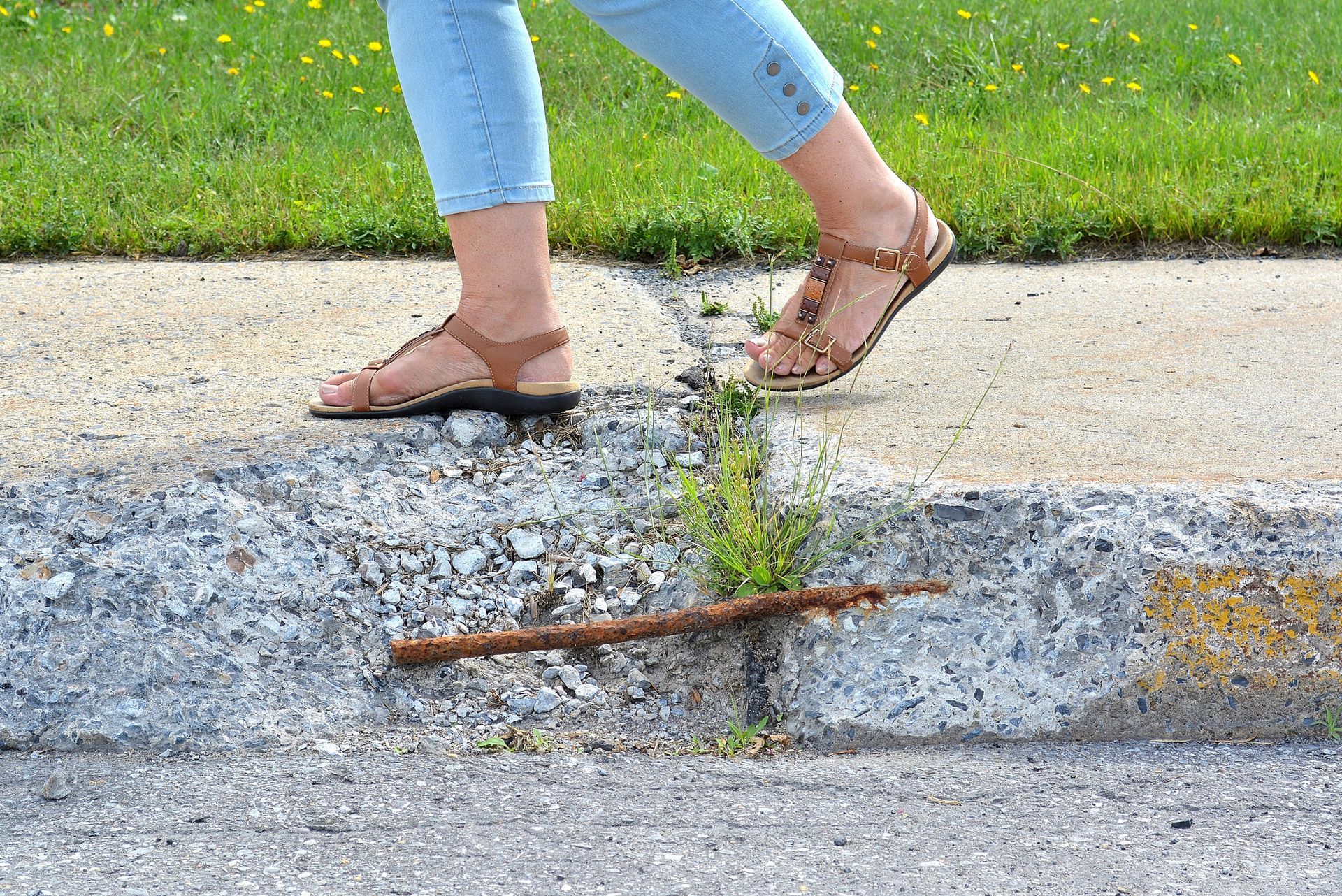 Close-up of a woman with sandals as she walks on a neglected and broken sidewalk. Close-up of a woman with sandals as she walks on a neglected and broken sidewalk.