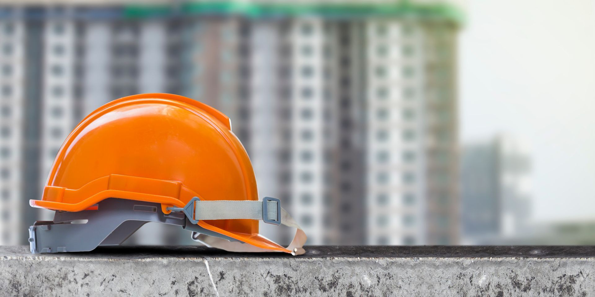 Orange construction helmet on concrete with blurred building in background. Orange construction helmet on concrete with blurred building in background.