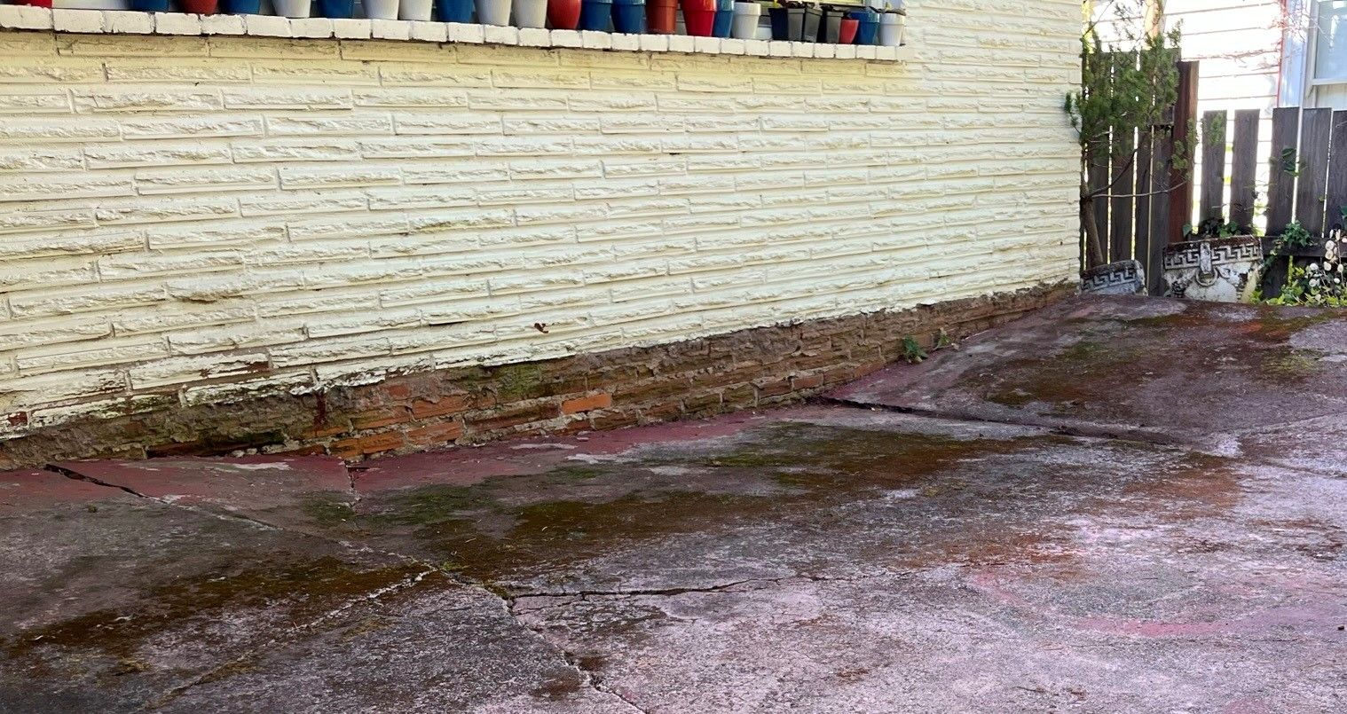 Wet, stained concrete next to a wall with a row of colorful flower pots. A wooden fence is at the right.