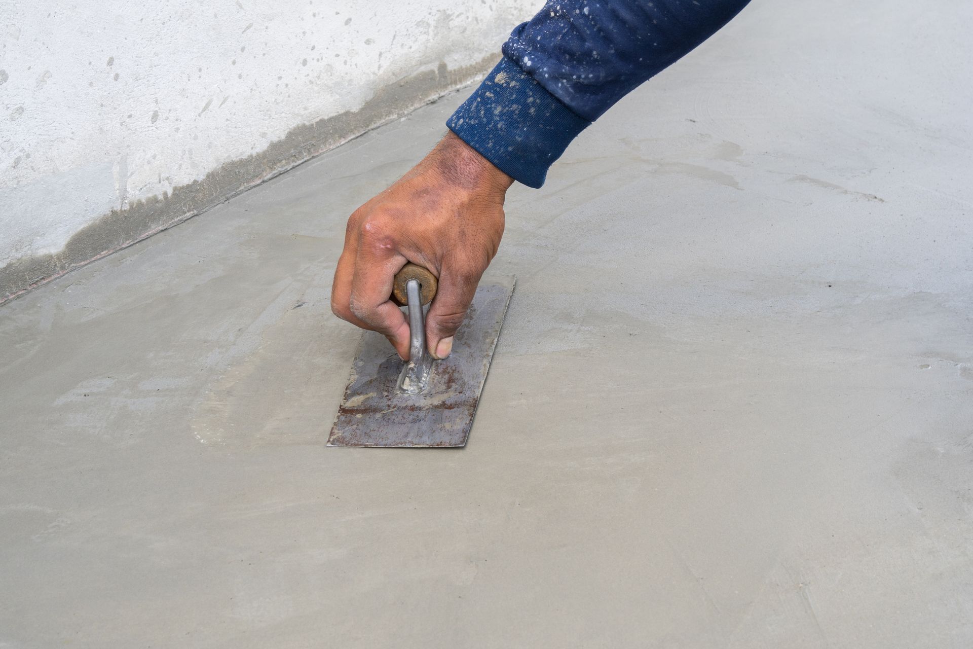 Hand smoothing wet cement with trowel on concrete surface.
