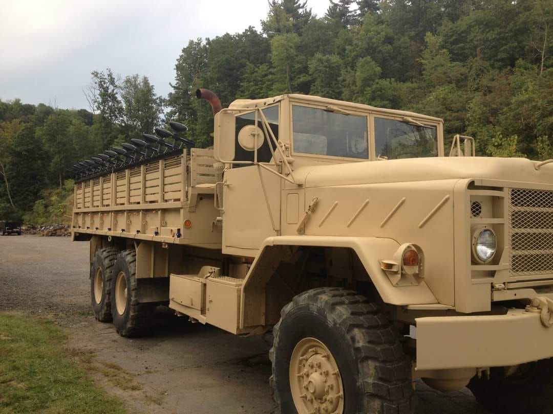 Tan military truck in wooded area.