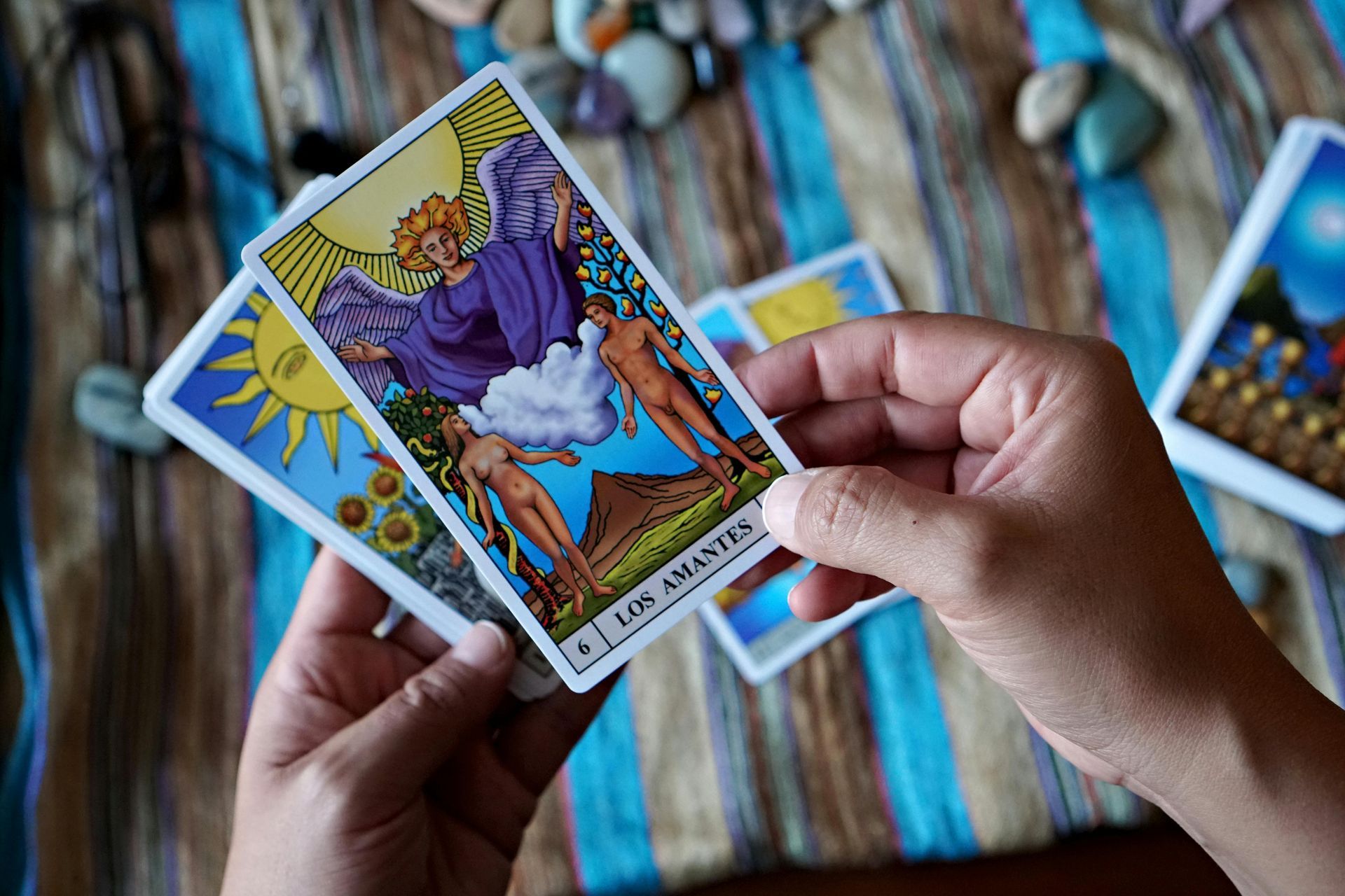 Hands holding a Tarot card with an angel figure, surrounded by other cards on a striped cloth.