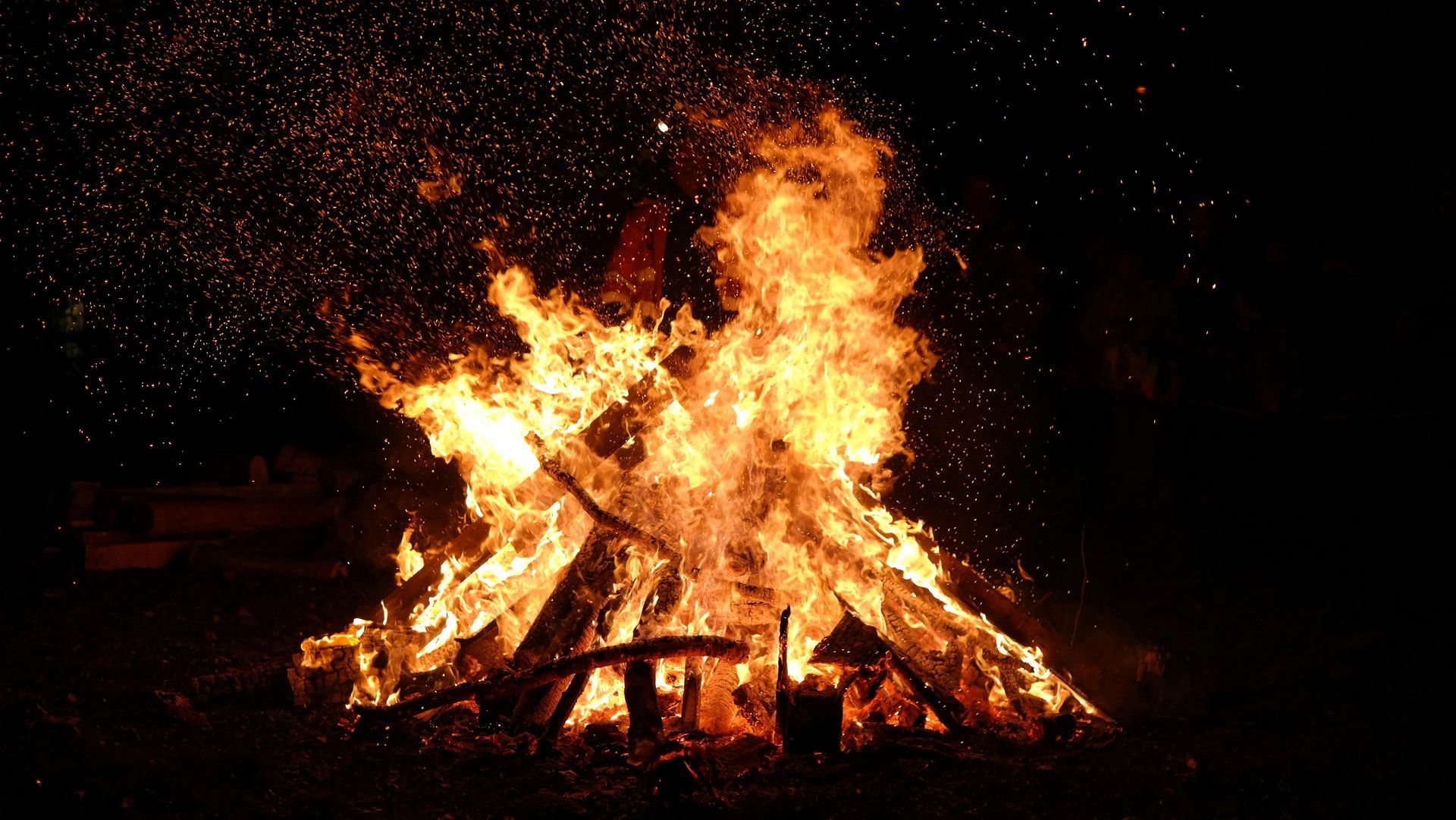 A roaring bonfire at night. Burning wood with orange and yellow flames and sparks against a dark background.