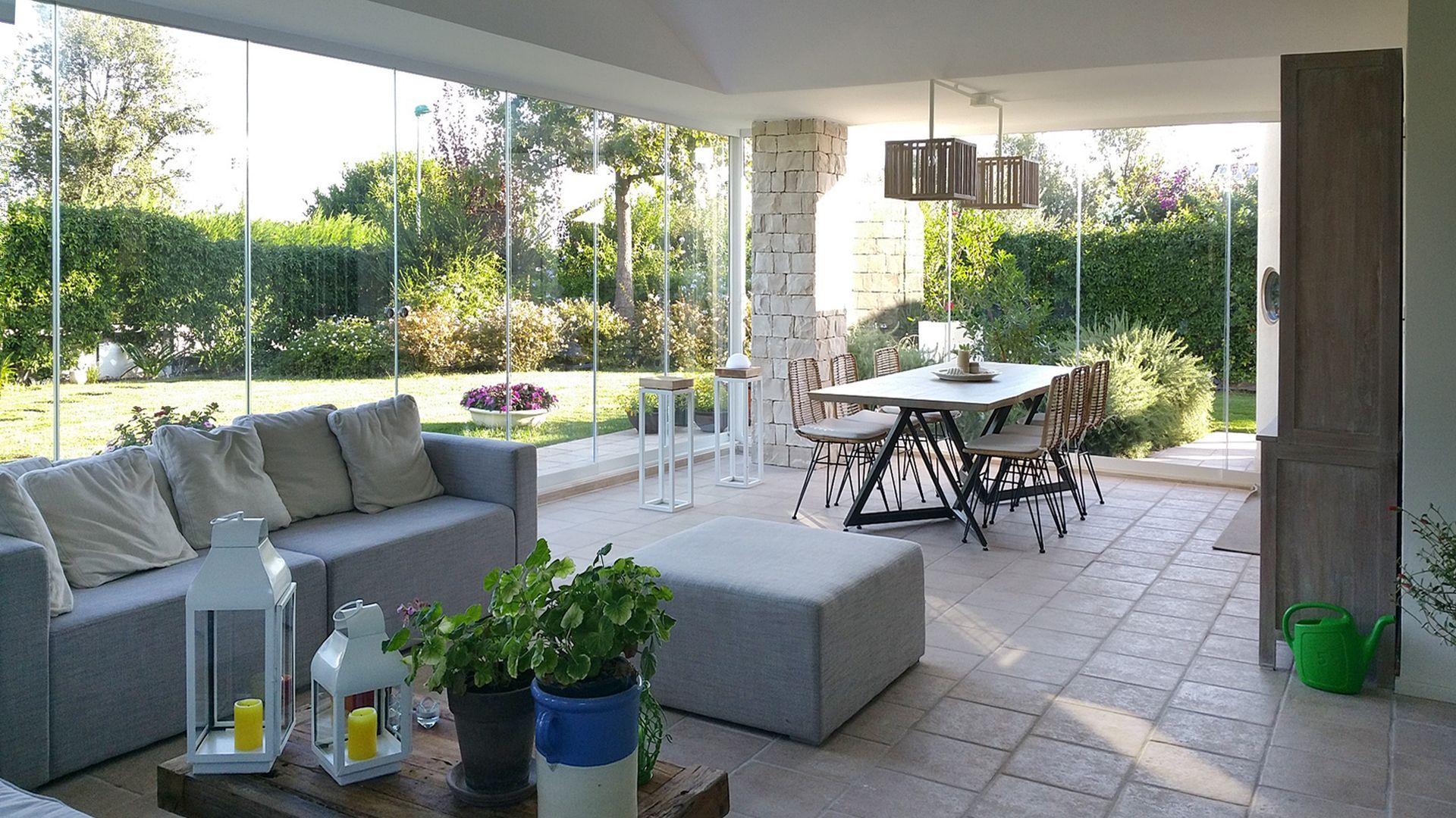 Ristorante con pareti in vetro, posti a sedere all'aperto con ombrellone, patio in pietra ed edifici sullo sfondo in una giornata di sole.