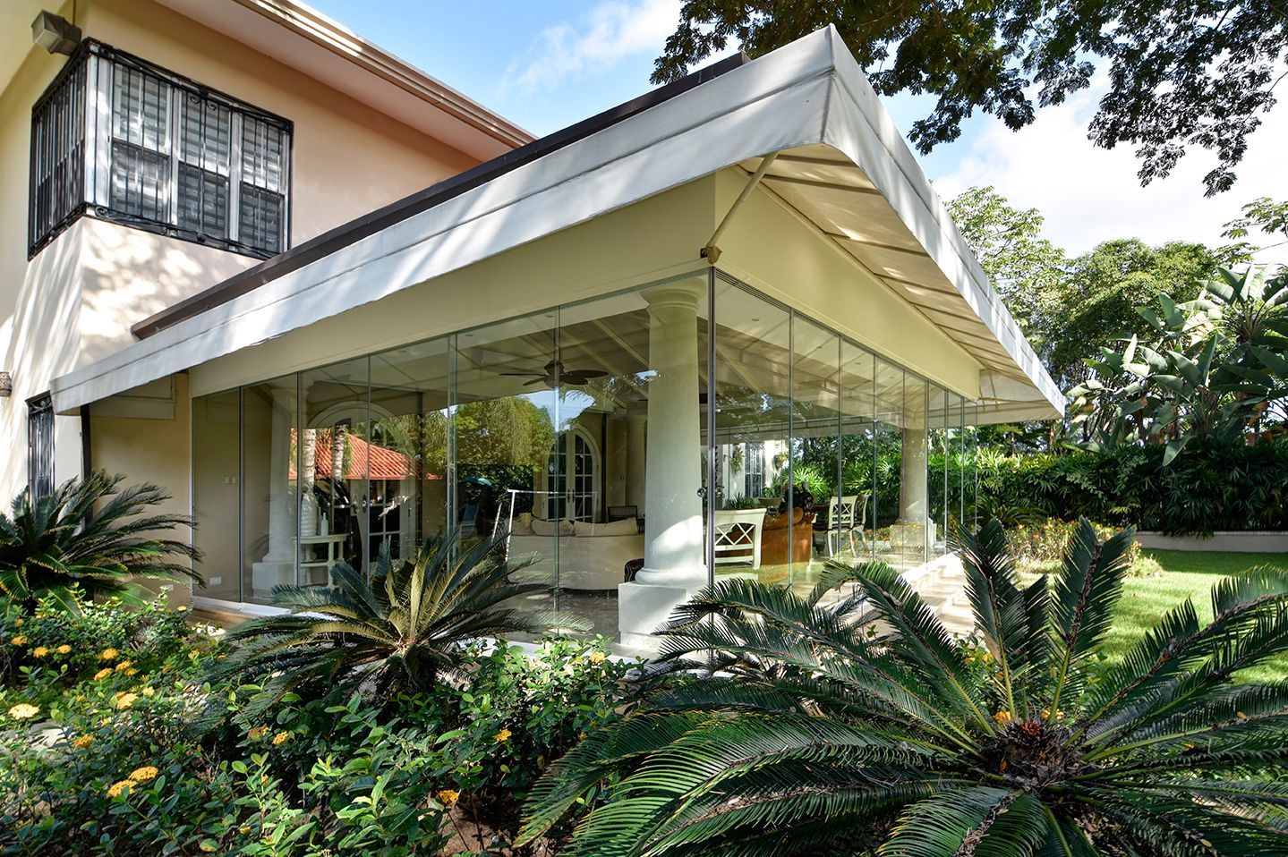 Piscina coperta con parete in vetro che si affaccia su un patio esterno, luce solare intensa e vegetazione.