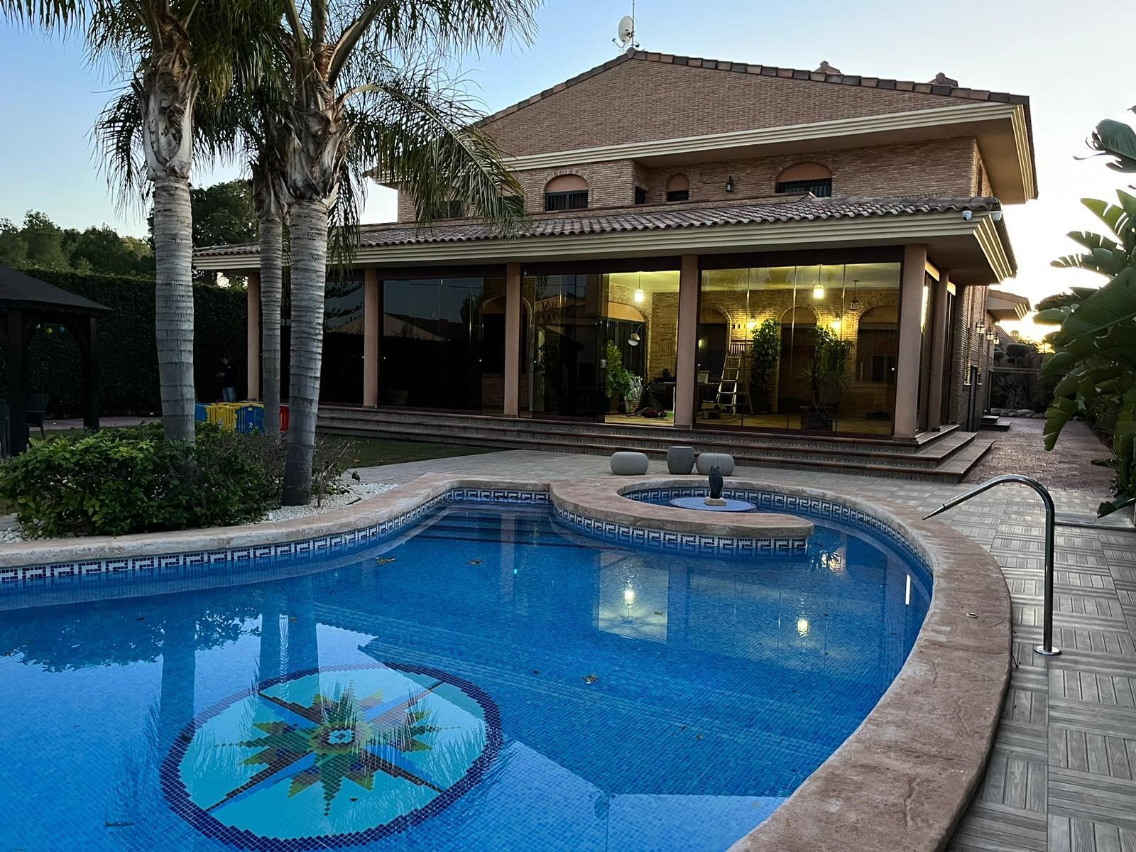 Un moderno ampliamento di un edificio con pareti in vetro, pilastri in mattoni, pavimento piastrellato e posti a sedere all'aperto.