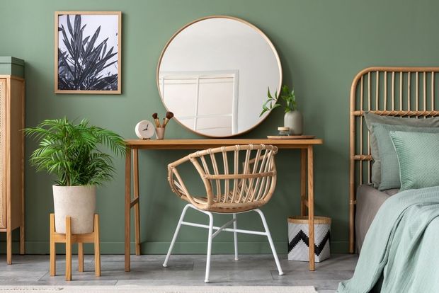 A bedroom with green walls , a desk with a chair and a mirror.