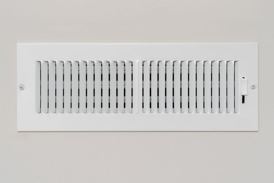 A white air vent is hanging on a white wall.