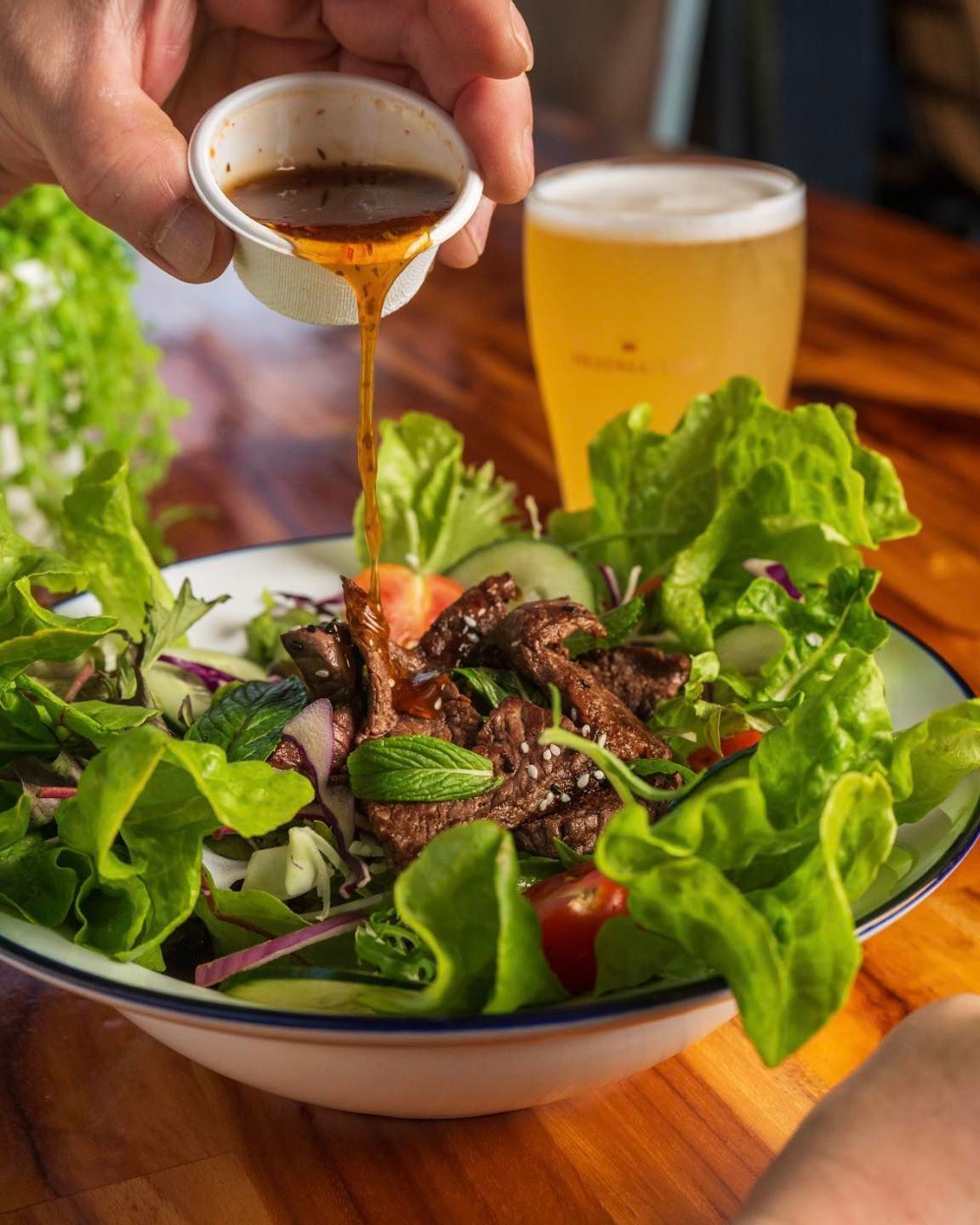A Person is Pouring Sauce on a Salad Next to a Glass of Beer — Chop ‘n Chill Raby Bay in Cleveland, QLD
