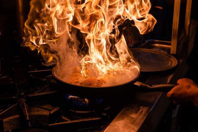 Person is Cooking Food in a Frying Pan on a Stove With Flames Coming Out of It — Chop ‘n Chill Raby Bay in Cleveland, QLD