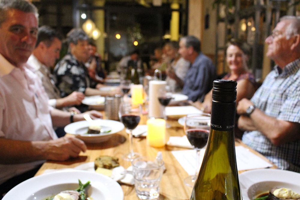 A Group of People Are Sitting at a Table With Plates of Food and a Bottle of Wine — Chop ‘n Chill Raby Bay in Cleveland, QLD
