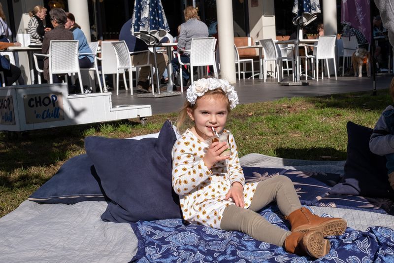 A Little Girl is Sitting on a Blanket Drinking From a Straw — Chop ‘n Chill Raby Bay in Cleveland, QLD