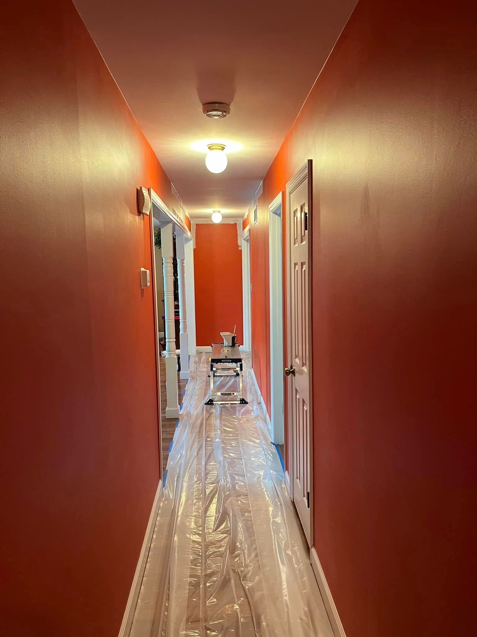 A long hallway with red walls and white trim is being painted.