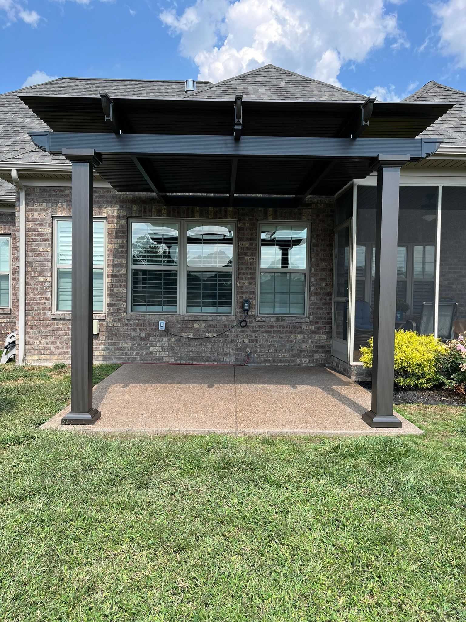 Pergola over a brick patio, with a view of a home and grassy yard