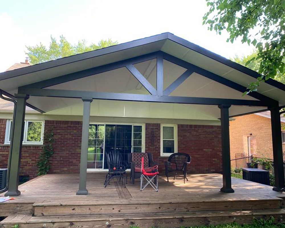 A patio with chairs and a table under a covered porch in front of a brick house.