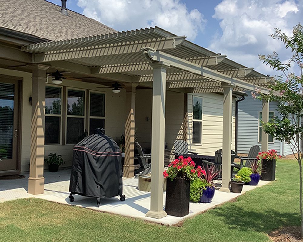 A patio with a pergola and a grill in front of a house.