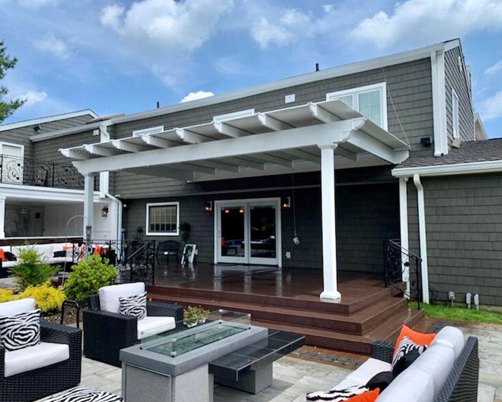 A patio with a pergola and a fire pit in front of a house.