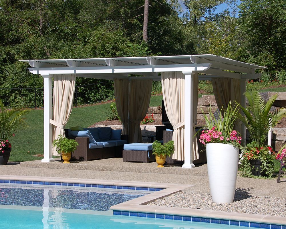 A pergola with a couch and ottoman sits next to a swimming pool