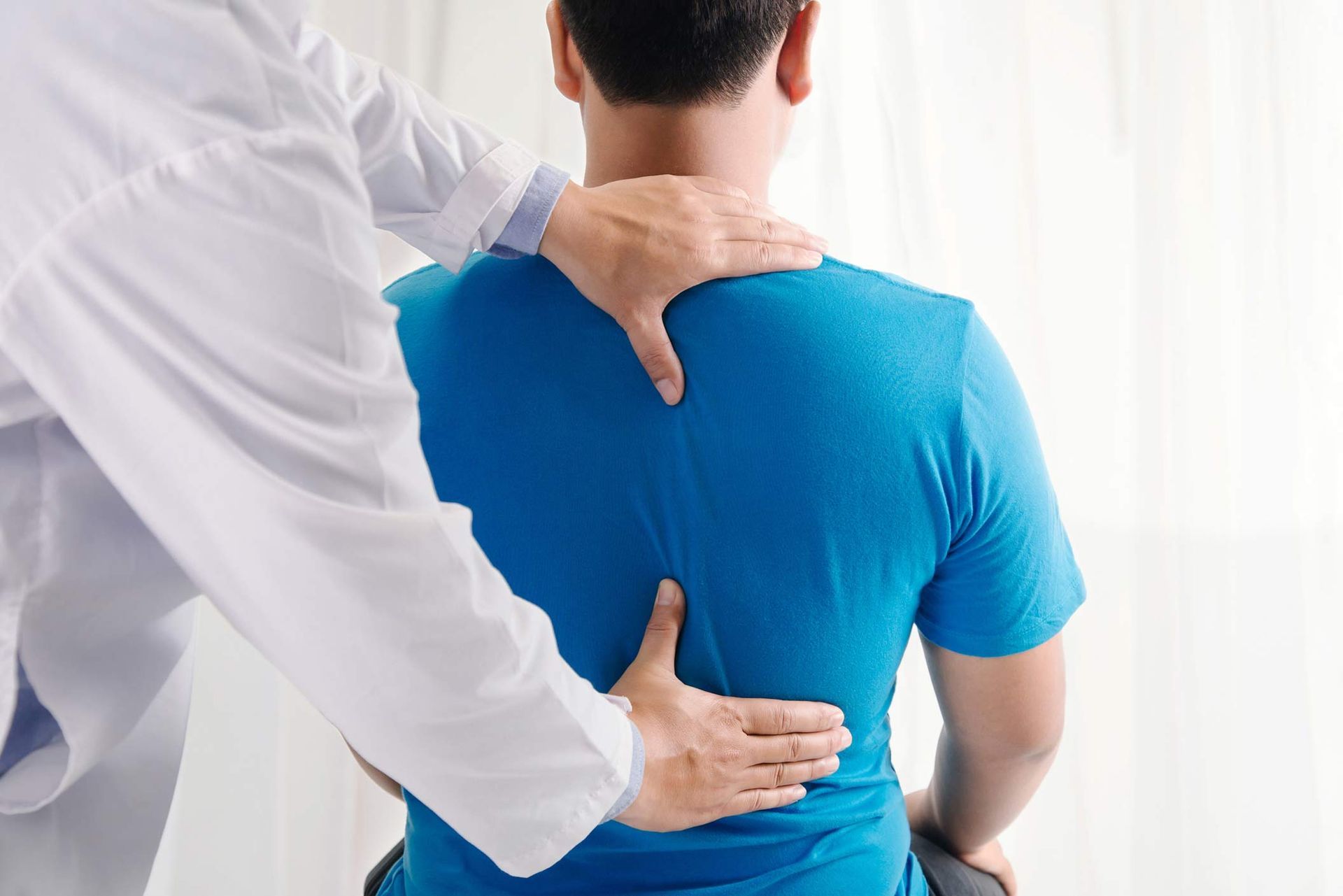 A doctor is examining a man 's back while he is sitting in a chair