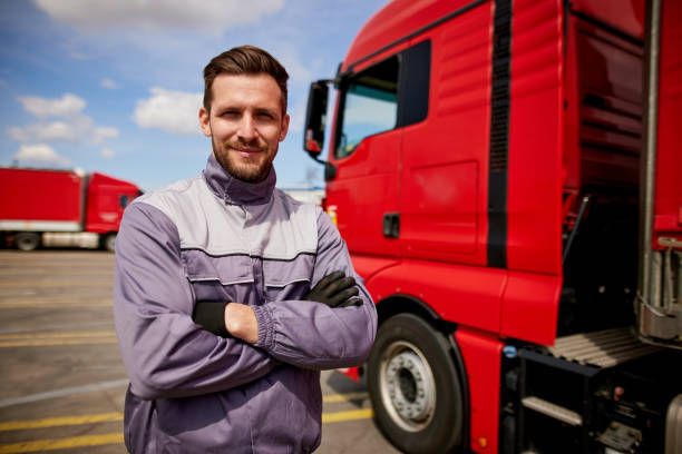 A man is standing in front of a red truck with his arms crossed