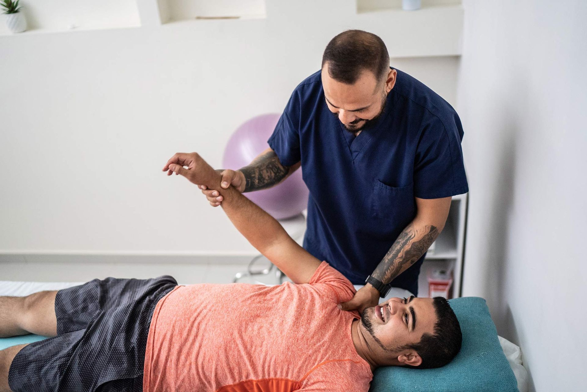 A man is laying on a bed while a doctor stretches his arm