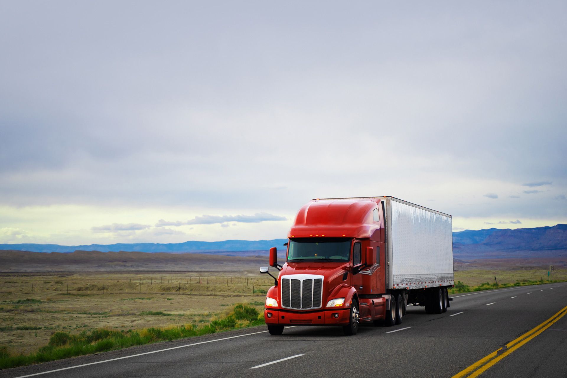 A red semi truck is driving down a highway in the desert