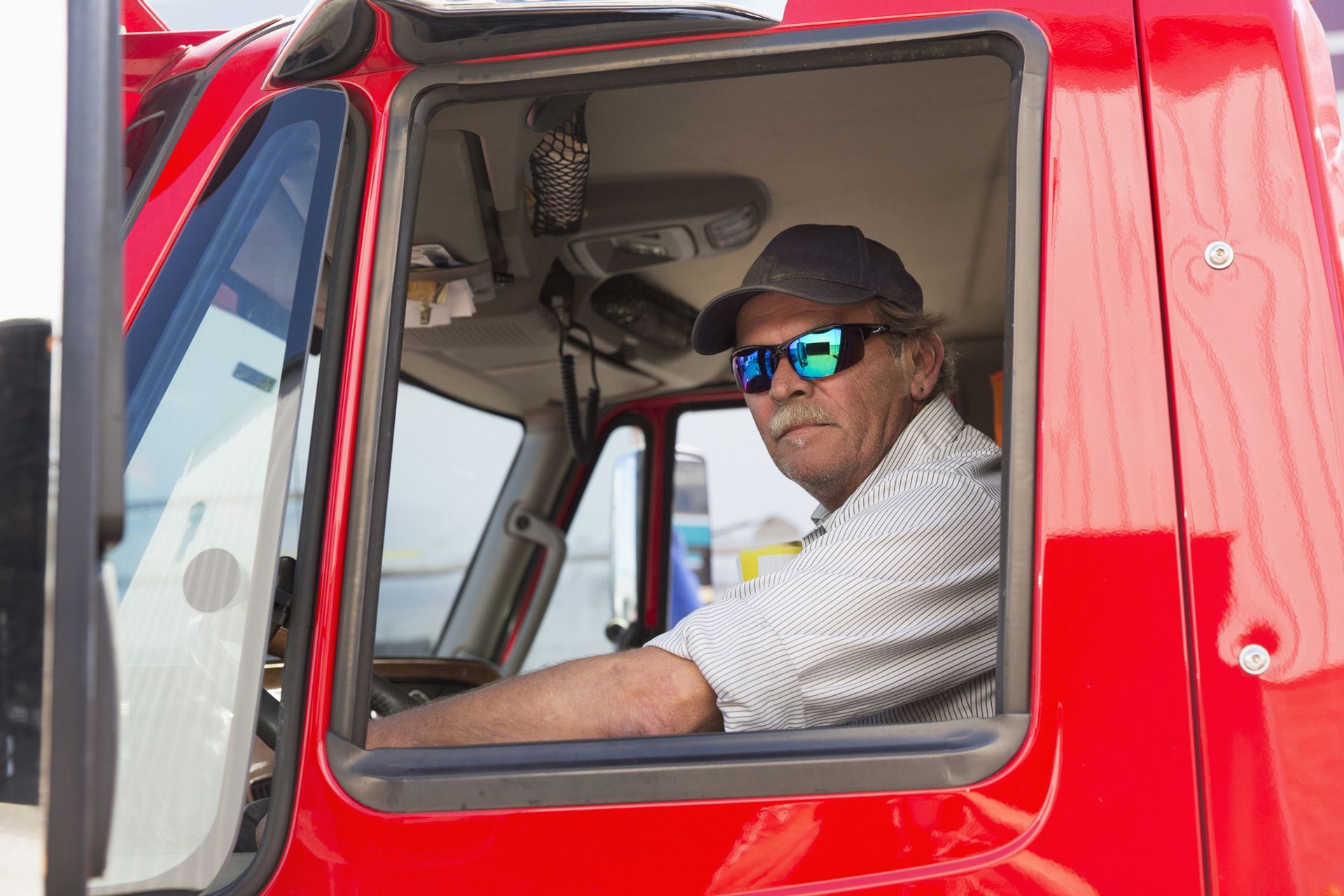 A man wearing sunglasses is sitting in the driver 's seat of a red truck