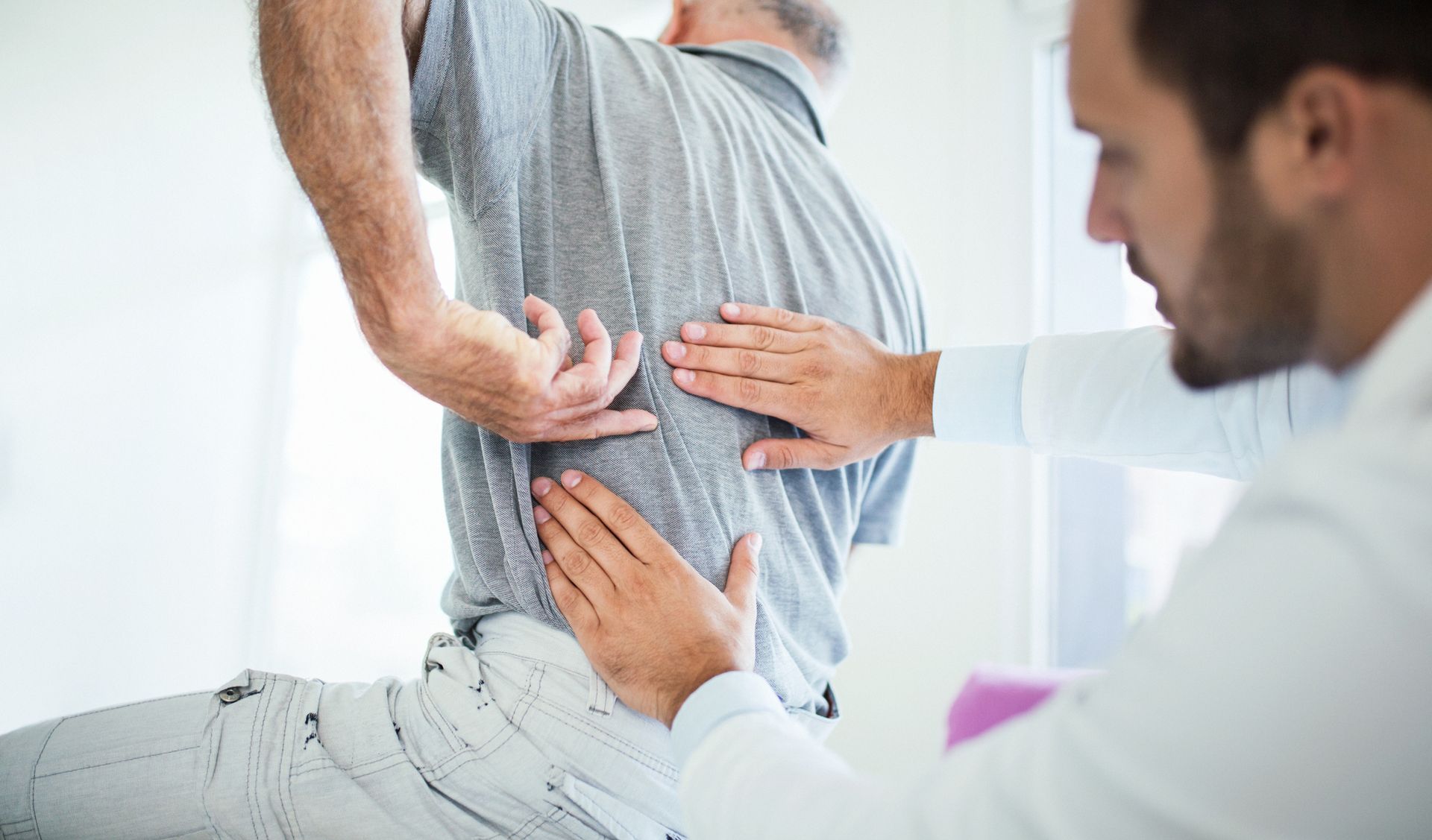 A doctor is examining a man 's back while he is sitting in a chair