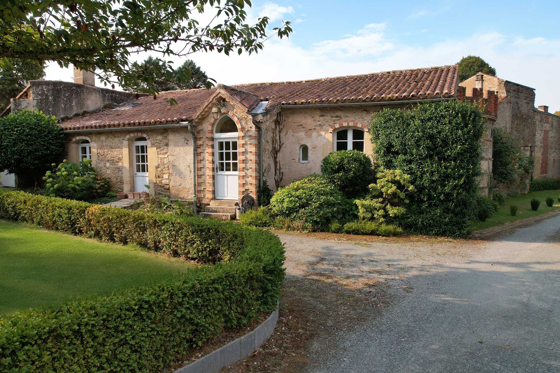 Stone house with a red tile roof, white doors, and a well-manicured lawn.