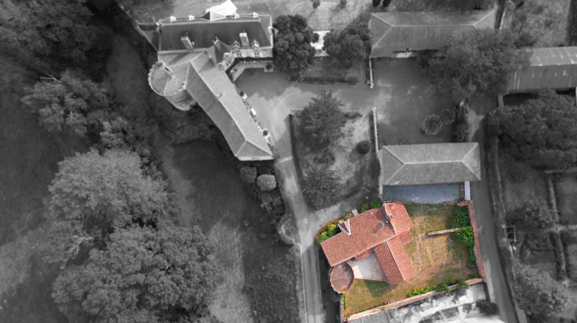 Aerial view of a building with an orange roof and green yard surrounded by black and white buildings and trees.